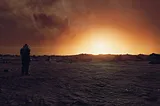 Screenshot of image taken in Starfield’s photo mode with playable character in a space suit to the left with back facing the camera, facing towards a bright sunrise on a barren landscape on Mercury.