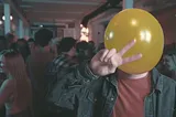Still image from the short film Air Head showing a man at a party with a yellow balloon for a head.