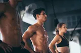 Two fit men and a woman working out at the gym.