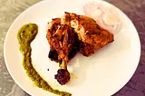 A plate of Tandoori Chicken with coriander chutney and onions.