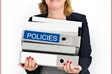 A photo of a business woman carrying a stack of binders, one of which is labeled as “policies.”