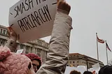 Photo of a person holding up a sign in a protest. The sign says “Smash the Patriarchy.”
