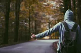 A young man stands on a roadside, hitching.