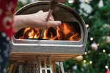 hands putting a pizza peel into a roccbox oven