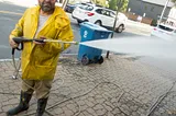 A man in a yellow slicker, scowling and holding a pressure sprayer.