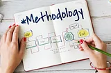 A photo of a page labeled Methodology with a flow diagram on it and a woman’s hands writing on the diagram.