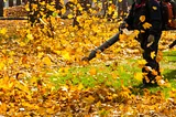 a stock photo of a man in dark clothes using a leaf blower