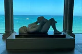 A sculpture of a woman lying down with the sea in the background.