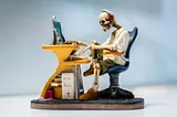 A figurine of human skeleton sitting infront of computer