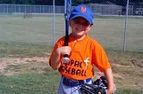 A photo of the author’s son holding a bat on his shoulder, a glove on his other hand and donning a New York Mets hat on his head. Smiling proudly.