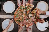 Birds eye view of a pizza, with several pairs of hands reaching for a slice.