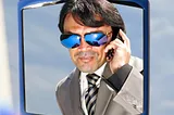 This is a picture of a douchey business guy wearing sunglasses and talking on a cellphone.