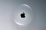 A transparent, floating liquid-glass sphere with the black Apple logo in the centre, set against a grey tiled background. The sphere subtly bends light around its edges.