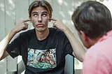 A teenager rolling his eyes and covering his ears while someone else is talking with him.