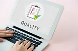 A photo of a person’s hands on a laptop computer with an image saying “quality” on the laptop’s screen.