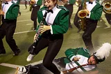 A high school marching band is caught in a sudden thunderstorm and a clarinet player is falling over another band member in the rain and the mud.