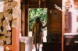 a woman walking out the door of a house, she is wearing a long brown coat and looking down