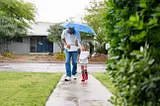 A man and young girl walk with an umbrella.