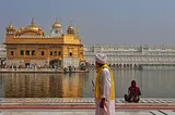 A golden sanctum is surrounded by water with an old devotee with turban and an Indian lady revering towards it.