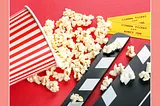 Composition with popcorn, movie slate, and cinema tickets on red background.