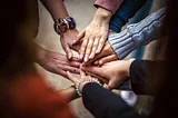 People putting their hands on top of eachothers’ hands while standing in a circle.