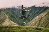 A woman jumping up in the air with mountains and a river in the background