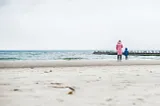 A mother and small boy pictured from behind, in the distance, standing on a beach looking out to sea.