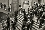 An image of a bustling crowd illustrating the constant motion and overwhelming pace of modern life. The visual conveys how we are bombarded with activity and stimuli, often becoming oblivious to our surroundings and the present moment. The image symbolizes the challenge of seeing through the noise and recognizing and overcoming suffering.