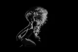 Black and white photo: female figure kneeling, a kind of fog or mist in front of her and hair in motion, wearing a swimsuit or a kind of leotard. (This is a much cooler photo than I’m making it sound. The figure is clearly in motion but I think that’s indicated by the appearance of the hair, and the mist or fog that looks displaced like something just moved through it.)