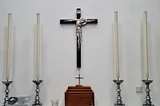 White wall, silver crucifix in the middle and two long candles unlit either side