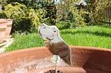 A paper dinosaur on a stick stuck into a plantless plant pot.