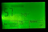 Photo of thermostat lit up by night green light showing 57 degrees with the heater off.