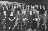 A large group of 20+ people in academic garb posing for a group photo in the late 1940’s. There are only a few women and all are Western.