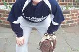 Little boy in baseball uniform, holding his glove while squatting down and looking into the camera