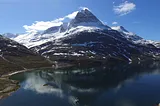 Drone photo of a sailboat anchored in the shadow of a snow-capped mountain in Greenland