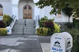 Picture of a ballot drop box in front of the steps of a white courthouse.