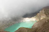 Brown and white cliffs surround a small, pale green lake. A foggy cloud moves diagonally across the photo