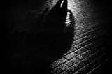 Long, threatening shadow of a man on wet, darkened pavement.