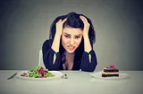 Woman tired of diet restrictions deciding whether to eat healthy food or sweet cake dessert she is craving isolated grey background. Human face expression emotion.