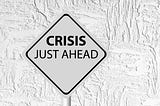 This os a black and white photo of a traffic warning sign saying “Crisis just ahead.”