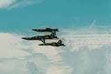 A group of three blue and yellow US navy fighter jets flying through a cloudy sky.