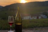 A bottle and glass of red wine with vineyards and sunset in the background