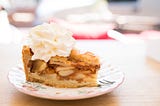 A picture of a slice of apple pie with whipped cream.