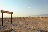 An image from Unsplash showing a desert landscape with a single, somewhat forlorn road sign saying “Sand Dunes” with an arrow pointing toward the horizon.