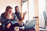 A couple smiles and waves at the camera on their laptop.