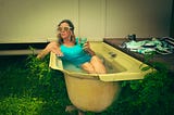 A woman relaxing in an old bathtub outdoors, holding a glass of wine