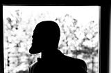 Silhouette of a pondering bald black man with a beard.