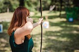 Woman aiming with a bow and arrow at a target.
