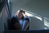 A photo of a despondent black woman sitting by the window in the stairwell.