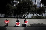 Activists hold signs and tombstone shapes in front of the Phillip Burton Federal Building to honor Covid-19 victims.